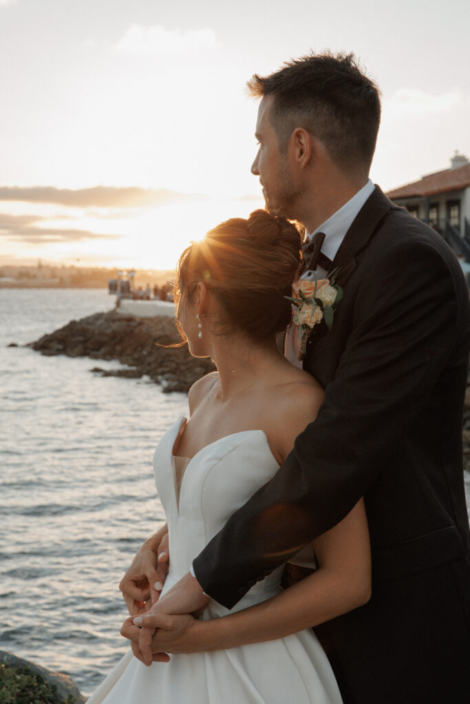 AJ and Janel embracing during golden-hour wedding portraits by the water