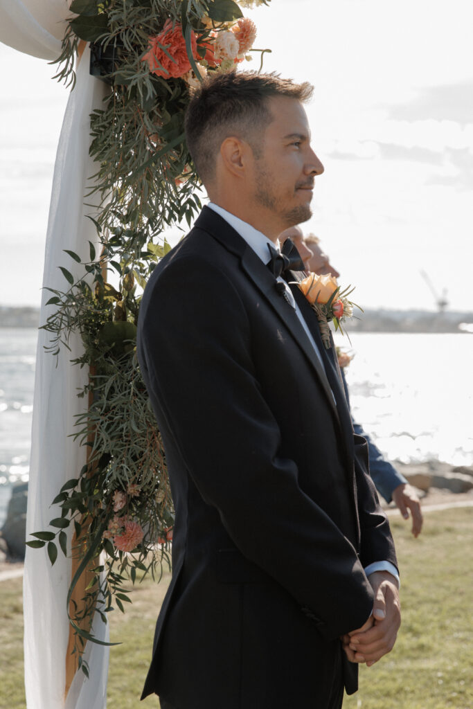 Groom standing beneath the floral ceremony arch during his Malibu Farm wedding