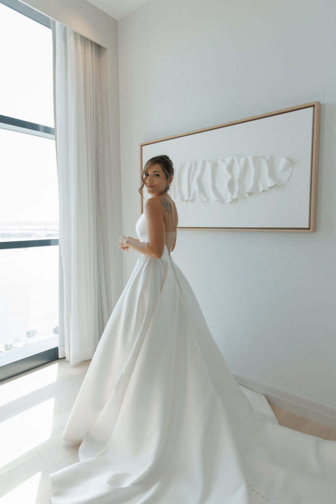 Bride standing in her wedding dress beside a window before the ceremony